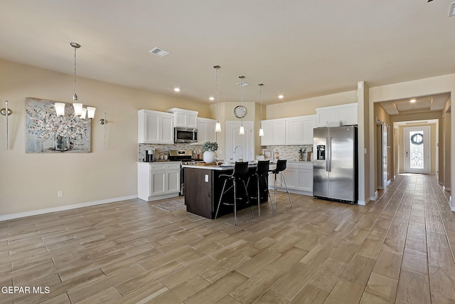 kitchen with a breakfast bar, hanging light fixtures, appliances with stainless steel finishes, an island with sink, and white cabinets