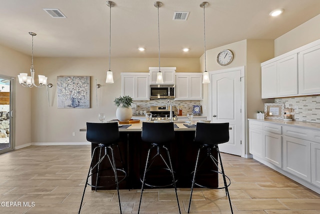 kitchen with white cabinetry, a center island with sink, a breakfast bar, and appliances with stainless steel finishes