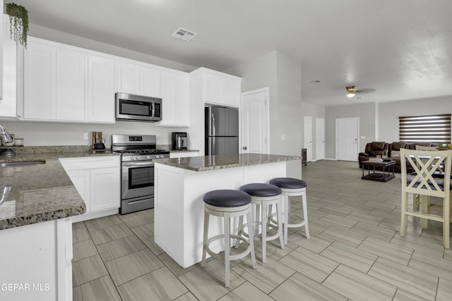 kitchen featuring sink, white cabinetry, a center island, dark stone countertops, and stainless steel appliances