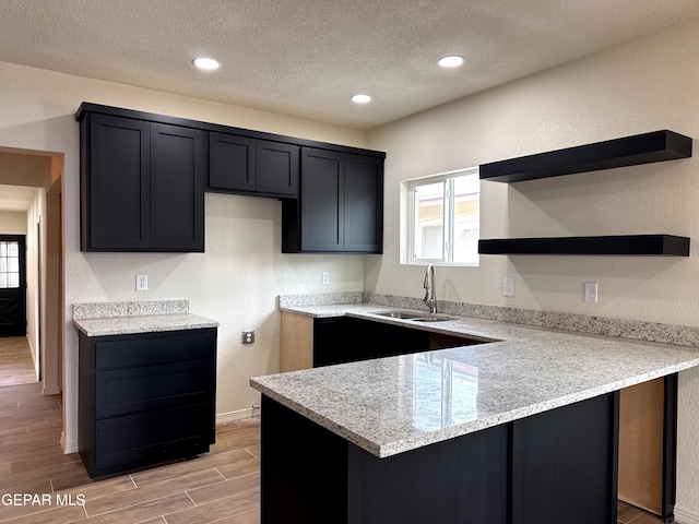 kitchen featuring a sink, open shelves, a textured ceiling, a peninsula, and wood tiled floor