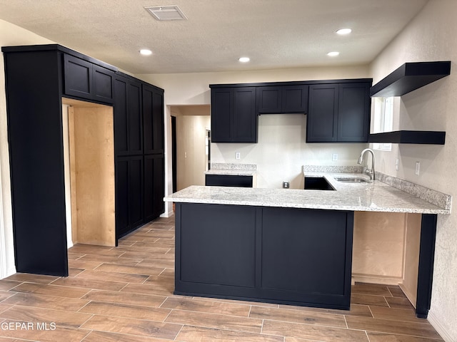 kitchen with visible vents, a peninsula, light stone countertops, a sink, and open shelves