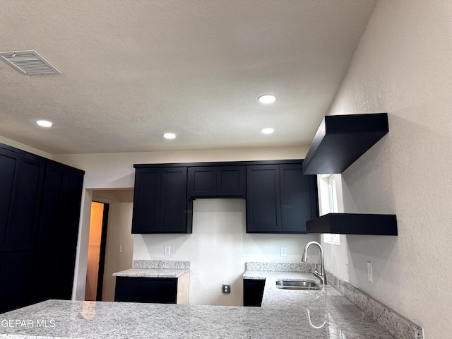 kitchen featuring a textured ceiling, visible vents, a sink, light stone counters, and a textured wall
