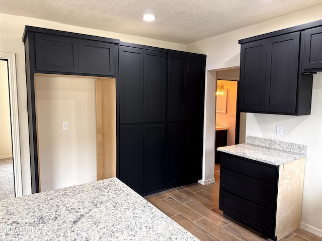 kitchen featuring a textured ceiling, light stone counters, baseboards, and wood finish floors