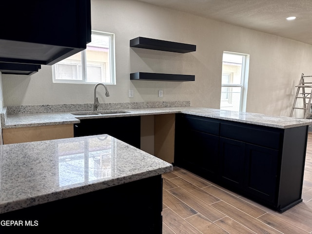 kitchen with wood finish floors, plenty of natural light, a peninsula, and light stone countertops