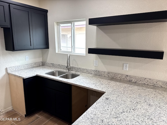 kitchen featuring light stone counters, a sink, open shelves, wood tiled floor, and a textured wall