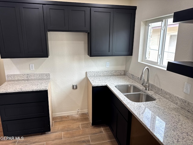 kitchen with a textured wall, baseboards, a sink, light stone countertops, and wood tiled floor