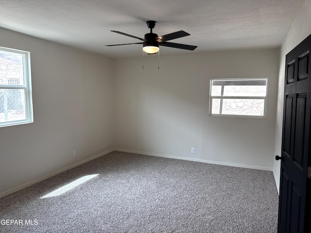carpeted empty room with a wealth of natural light, a ceiling fan, baseboards, and a textured ceiling