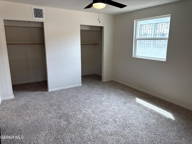 unfurnished bedroom featuring carpet, baseboards, multiple closets, visible vents, and a ceiling fan