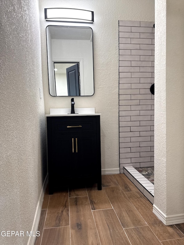 bathroom with baseboards, wood tiled floor, tiled shower, and vanity