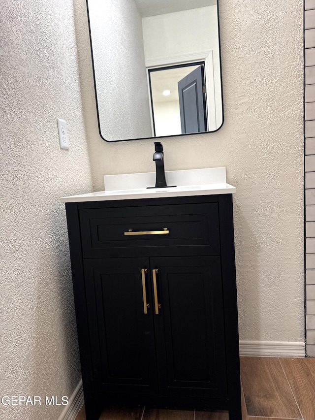 bathroom featuring baseboards, a textured wall, wood finish floors, and vanity