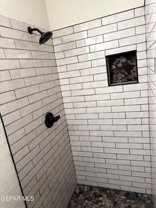 bathroom with a textured wall and tiled shower