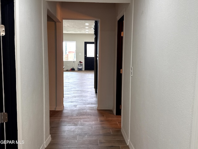 hall featuring baseboards, wood finished floors, and a textured wall
