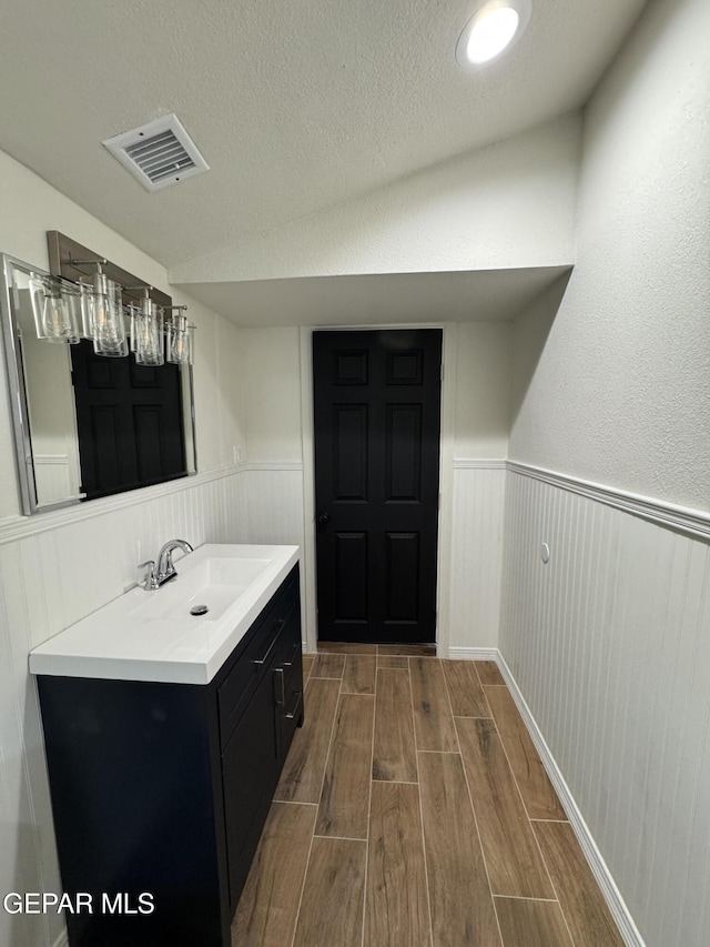 bathroom featuring a textured ceiling, visible vents, wood finish floors, vanity, and wainscoting