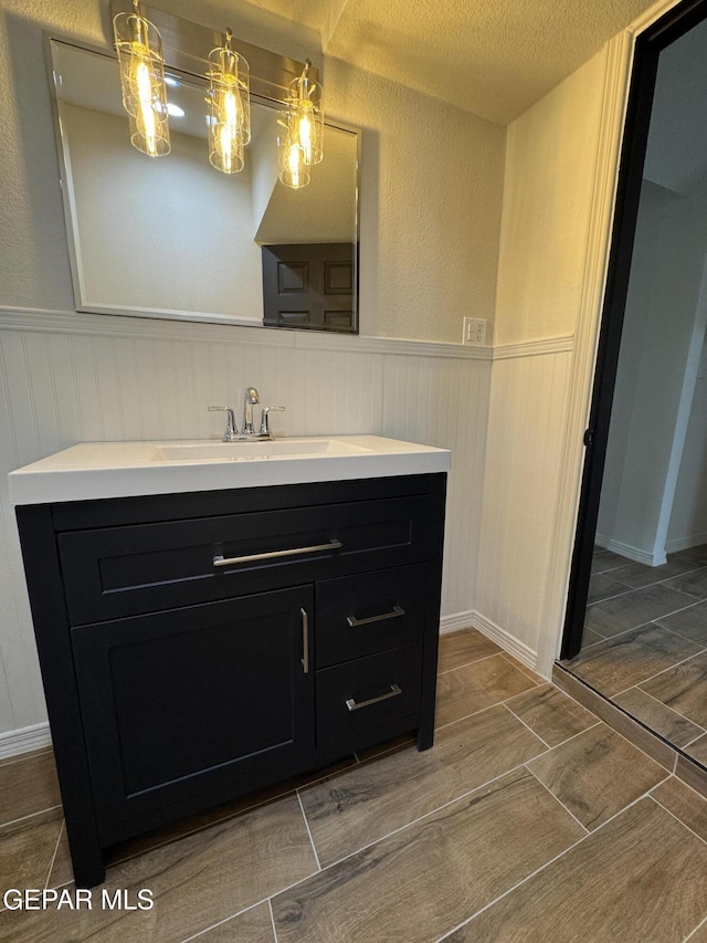 bathroom with a wainscoted wall, vanity, wood tiled floor, and a textured ceiling