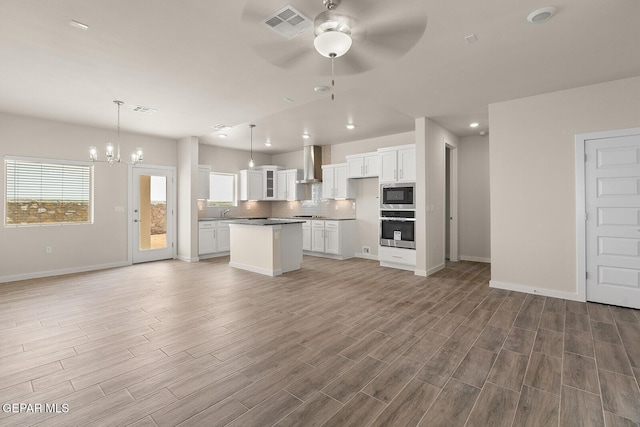 kitchen featuring built in microwave, oven, hanging light fixtures, and wall chimney range hood