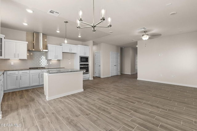 kitchen with pendant lighting, white cabinetry, stainless steel appliances, a center island, and wall chimney exhaust hood