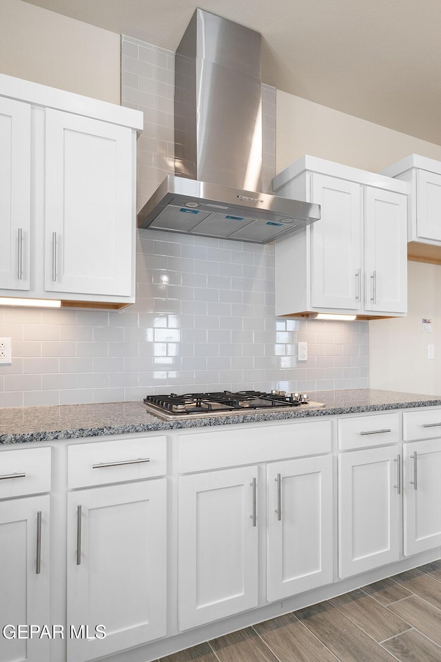 kitchen with white cabinetry, wall chimney range hood, decorative backsplash, and light stone countertops