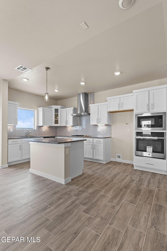 kitchen featuring white cabinetry, wall chimney exhaust hood, oven, and a kitchen island