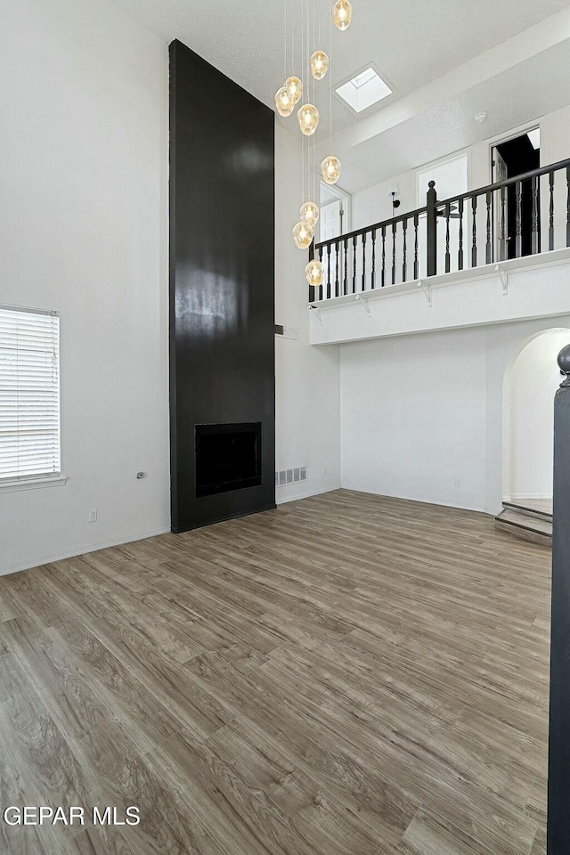 unfurnished living room featuring a skylight, hardwood / wood-style flooring, a fireplace, and a towering ceiling