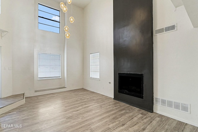 unfurnished living room featuring light hardwood / wood-style flooring, a large fireplace, and a high ceiling