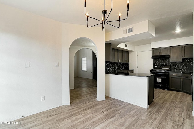 kitchen with black range oven, decorative backsplash, a notable chandelier, kitchen peninsula, and light hardwood / wood-style flooring