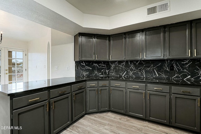 kitchen featuring tasteful backsplash, kitchen peninsula, dark stone counters, and light wood-type flooring