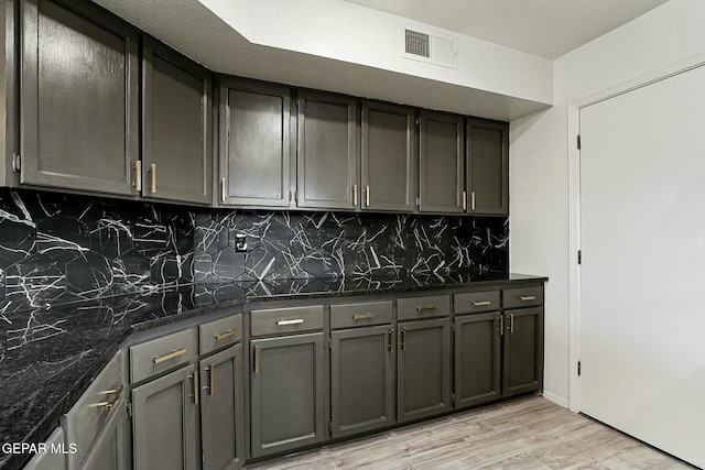 kitchen featuring light wood-type flooring, decorative backsplash, and dark stone countertops