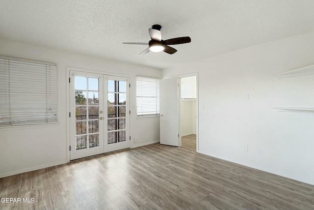 empty room with ceiling fan, light hardwood / wood-style flooring, french doors, and a textured ceiling