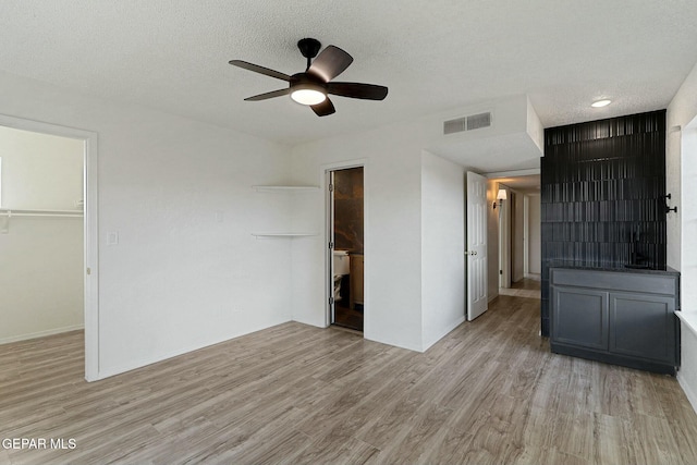 unfurnished bedroom with a walk in closet, light hardwood / wood-style floors, a closet, and a textured ceiling