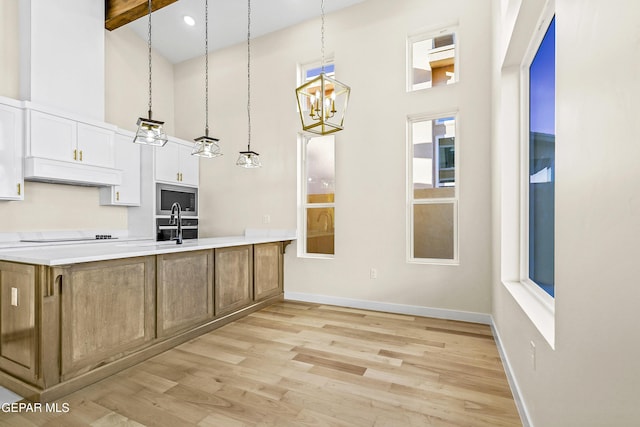 kitchen with premium range hood, built in microwave, white cabinetry, hanging light fixtures, and light hardwood / wood-style floors