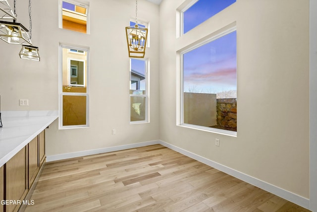 unfurnished dining area featuring a towering ceiling, a healthy amount of sunlight, a chandelier, and light hardwood / wood-style flooring