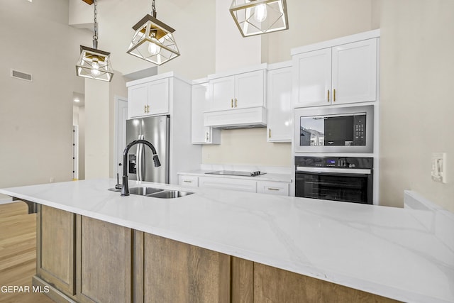 kitchen featuring sink, white cabinetry, a kitchen island with sink, black appliances, and decorative light fixtures