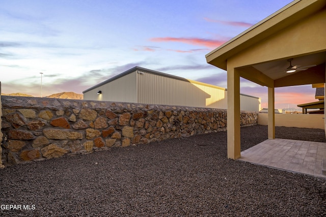 yard at dusk with ceiling fan and a patio area