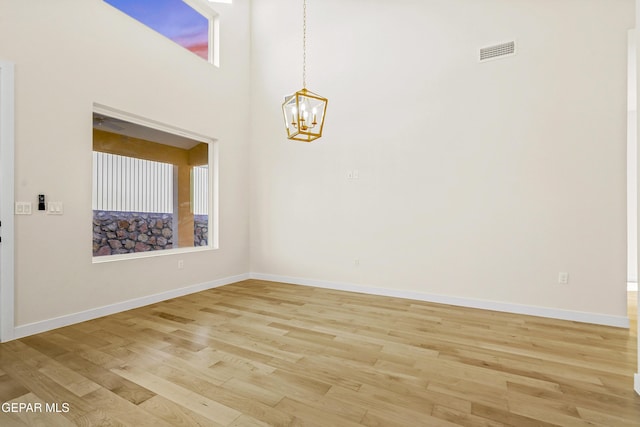 unfurnished room featuring a towering ceiling, light hardwood / wood-style flooring, and a chandelier