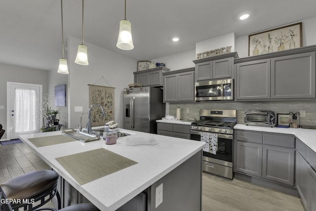 kitchen with stainless steel appliances, gray cabinets, a kitchen island with sink, and hanging light fixtures