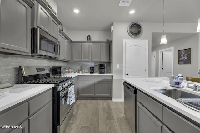 kitchen with gray cabinets, backsplash, stainless steel appliances, decorative light fixtures, and light wood-type flooring