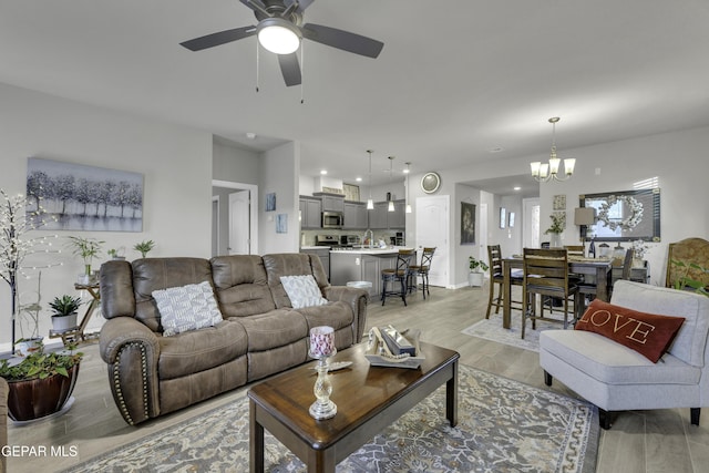 living room with ceiling fan with notable chandelier and light hardwood / wood-style floors