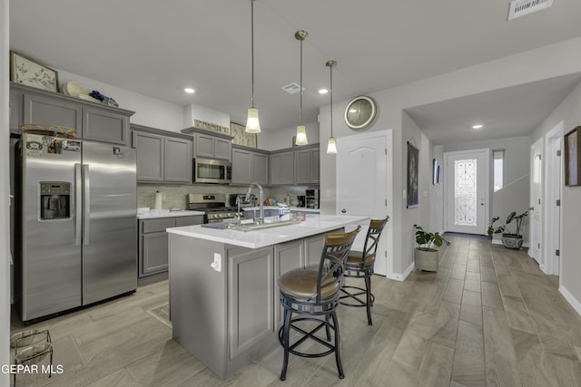 kitchen featuring gray cabinets, a breakfast bar area, hanging light fixtures, a kitchen island with sink, and stainless steel appliances