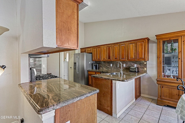 kitchen featuring sink, range, stainless steel fridge with ice dispenser, kitchen peninsula, and dark stone counters