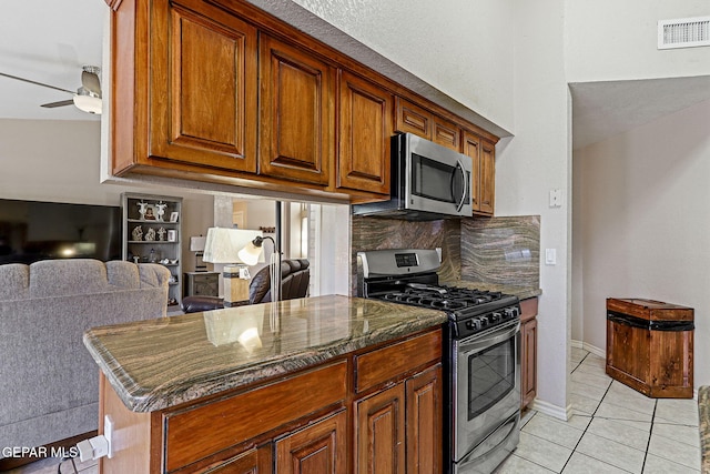 kitchen featuring light tile patterned flooring, appliances with stainless steel finishes, decorative backsplash, dark stone counters, and ceiling fan