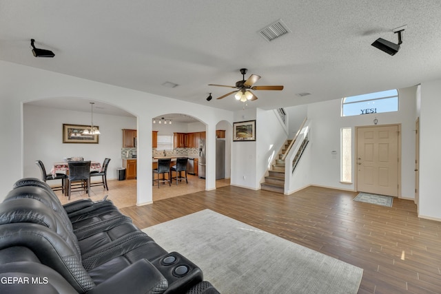 living room featuring ceiling fan with notable chandelier, wood-type flooring, and a textured ceiling