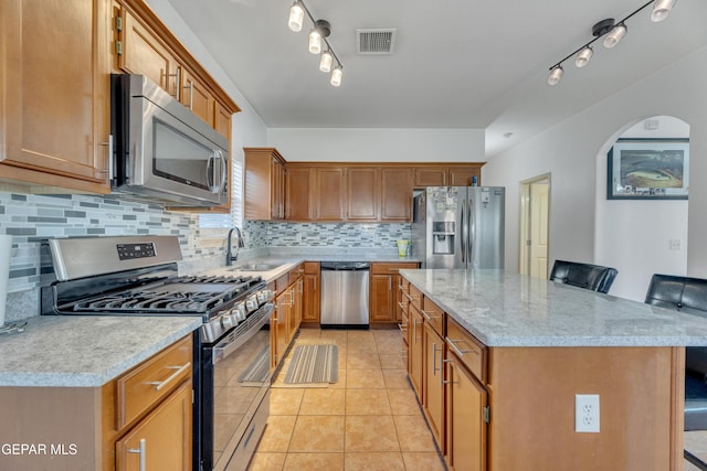 kitchen with sink, light tile patterned floors, appliances with stainless steel finishes, a kitchen breakfast bar, and backsplash