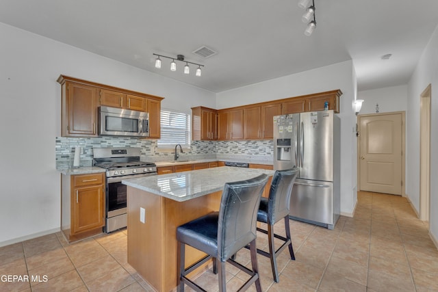 kitchen featuring a breakfast bar, appliances with stainless steel finishes, backsplash, light stone counters, and a kitchen island