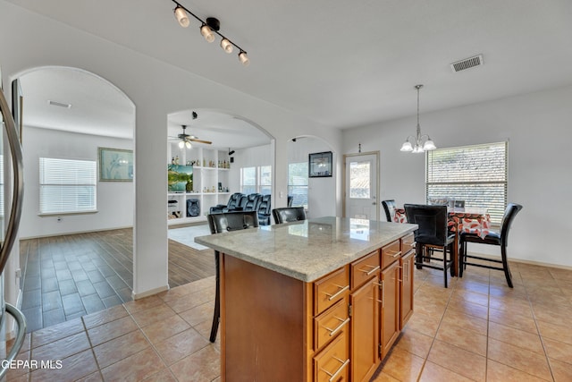 kitchen featuring light tile patterned flooring, light stone counters, decorative light fixtures, a kitchen island, and ceiling fan with notable chandelier