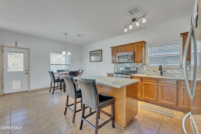 kitchen with sink, hanging light fixtures, appliances with stainless steel finishes, a kitchen island, and decorative backsplash