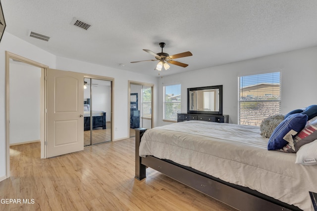 bedroom featuring multiple closets, ceiling fan, a textured ceiling, and light hardwood / wood-style floors