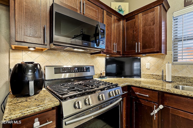 kitchen with light stone countertops, appliances with stainless steel finishes, and decorative backsplash