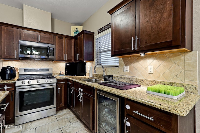 kitchen with wine cooler, sink, appliances with stainless steel finishes, light stone countertops, and backsplash