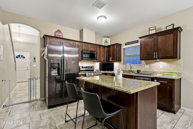 kitchen with a breakfast bar, stainless steel appliances, a center island, light stone counters, and decorative backsplash