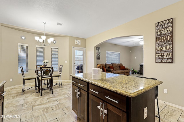 kitchen with pendant lighting, a center island, light stone counters, a kitchen bar, and ceiling fan with notable chandelier